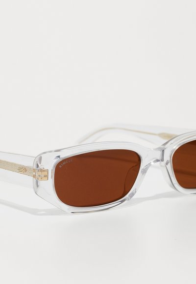Clear frame sunglasses with brown lenses, featuring textured gold accents on the temples. Angular design, lightweight materials.