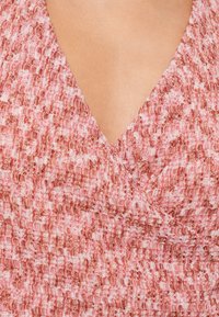 Rosa och röd texturerad tyg med en V-ringning, med subtila ränder och ett mjukt, vävt utseende.