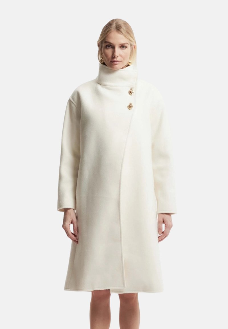 Cappotto bianco in lana con colletto alto, maniche lunghe e chiusura diagonale. Presenta due bottoni floreali in tono oro come dettagli.