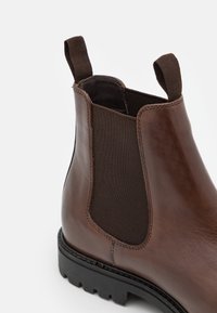 Botín Chelsea de cuero marrón con paneles laterales elásticos, una asa y suela de goma texturizada para mayor agarre y durabilidad.
