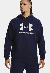 Felpa con cappuccio blu navy in pile, dotata di una tasca frontale e grande logo Under Armour bianco sul petto.