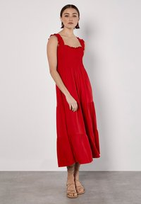 Rotes Maxikleid mit gesmoktem Oberteil, Rüschenträgern und gestuftem Rock. Gefertigt aus einem leichten Stoff, mit fließender Silhouette und weichem Textil.