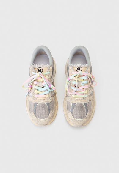 Μπεζ και γκρι αθλητικά παπούτσια με λουλουδάτα σχέδια, ξεφτισμένες άκρες και κορδόνια σε παστέλ ουράνιο τόξο δεμένα σε φιόγκους, σε θέα από πάνω πάνω σε φωτεινό φόντο.