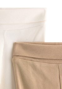 Leggings a coste in bianco sporco e beige, con ampi elastici in vita. La texture del tessuto è morbida, con una finitura leggermente elasticizzata.