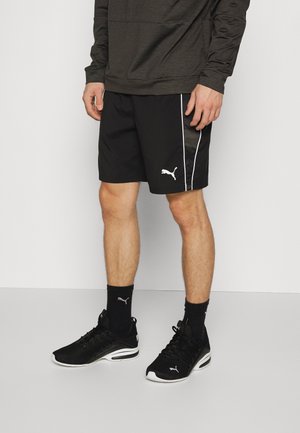 Schwarze Sportshorts mit weißen Seitenstreifen und einem kleinen Logo. Getragen mit schwarzen Sneakern und schwarzen Socken. Der Stoff scheint leicht und atmungsaktiv zu sein.