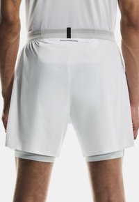 Shorts de sport blancs avec une ceinture élastique grise, présentant un design en maille avec de petits trous. Comprend une doublure intérieure ajustée.