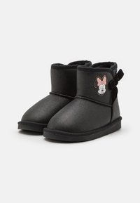 Botines de tobillo para niña pequeños, en color negro y hechos de un material suave, con un emblema de Minnie Mouse en rosa y un lazo en el lateral. Forro interior suave.