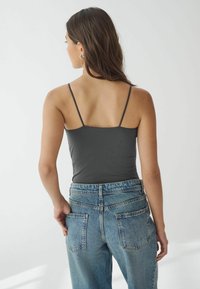 Grå tætsiddende tanktop med tynde stropper, parret med højtaljede lyseblå denimjeans med klassisk femlomme-design og frynsede kanter.