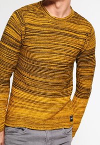 Pletený svetr s vodorovnými pruhy v odstínech hořčicové žluté a tmavě hnědé. Design s okrouhlým výstřihem, texturovaná látka, s malou značkovou nášivkou na lemu.