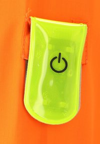 Un textile orange à surface texturée comporte une poche transparente vert clair contenant un symbole d'alimentation noir.