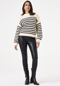 Chunky knit sweater in cream with black horizontal stripes, ribbed hem and cuffs. Paired with black faux leather pants and ankle boots.