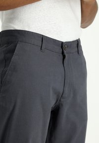 Los pantalones azul marino presentan un cierre frontal con cremallera y botón, con una textura suave y costuras bien cosidas. Diseño minimalista con bolsillos inclinados.