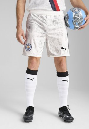 Hvide fodboldshorts med et marmorprint, Manchester City-logo, sorte accenter, parret med sorte støvler og hvide knælange sokker.