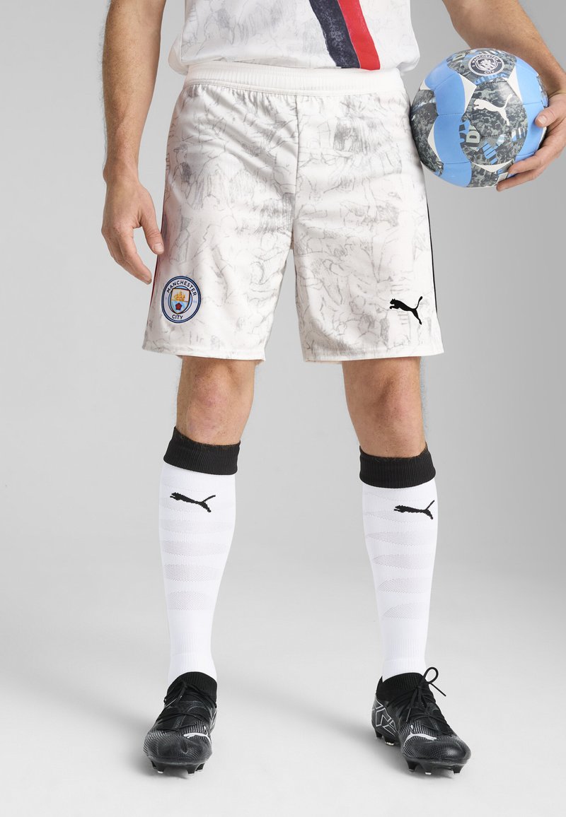 Valged jalgpallishortsid marmoriga kaunistatud, Manchester City logo, mustad aktsendid, koos mustade spordijalatsite ja valgete kõrgete sokkidega.