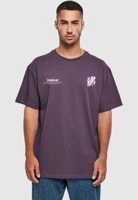 Lila Baumwoll-T-Shirt mit kurzen Ärmeln, Rundhalsausschnitt und weißem Drucktext auf der Vorderseite. Lässige Passform und gerippte Textur.