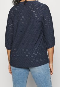 Navy blue blouse with a textured eyelet pattern, three-quarter sleeves, and a loose fit. Accent details highlight the design.