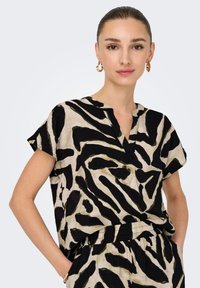 Kortermet topp i beige med et dristig svart zebra-mønster. Har V-hals og løs passform, laget av myk, teksturert stoff.