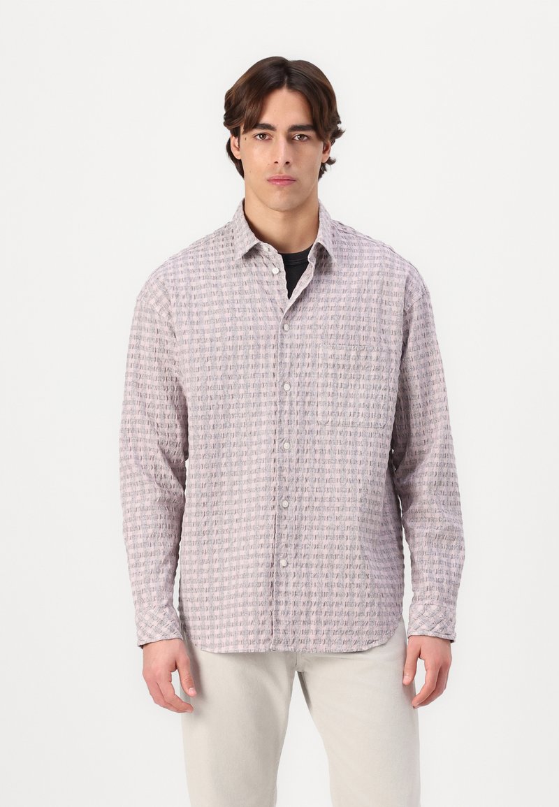 Long-sleeve button-up shirt in light pink with textured pattern, featuring a collar and button closure, worn over a black shirt.
