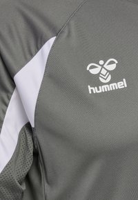 Tissu de sport gris avec une bande chevron blanche et un logo hummel blanc représentant un bourdon stylisé sur la zone de la poitrine.