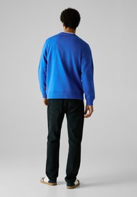 Blauwe crewneck sweatshirt gemaakt van een katoenmix, met lange mouwen. Gecombineerd met zwarte denim jeans en beige sneakers met marineblauwe accenten.
