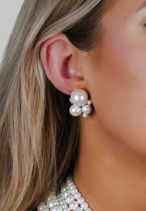 Weiße Perlenohrringe mit einer Cluster-Design, das mehrere Größen von Perlen zeigt, vor einem strukturierten Hauthintergrund. Elegant und zusammenhängend.