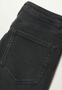 Jeans de mezclilla negra con un bolsillo trasero visible, que presentan costuras en contraste y una textura suave. La tela parece duradera y resistente.