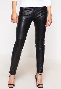 Svarta läderbyxor med smal passform, med dragkedjefickor och dragkedjor vid anklarna. Slät textur med knäpaneler för extra designdetalj.