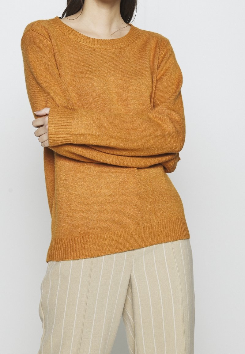 Maglione giallo senape con scollo tondo, maniche lunghe e polsini e orlo a coste. Il tessuto appare morbido con una sottile trama.