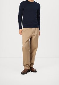 Marineblauer Strickpullover, beigefarbene gerade geschnittene Hose, braune Lederschuhe. Schlichtes Design mit Rundhalsausschnitt und ohne sichtbare Muster oder Akzente.