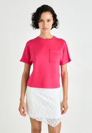 Fuchsia cotton t-shirt with short sleeves and a chest pocket, paired with a white lace skirt that is knee-length with an asymmetrical hem.