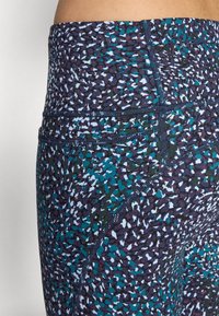 Többszínű, aktív viseletre szánt leggings, texturált mintázattal sötétkék, zöld és fehér színekben, magas derékkal és megerősített varratokkal.