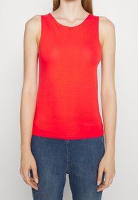 Röd ärmlös topp i ett mjukt tyg, med rund halsringning och en figursydd form. Parat med blå denimjeans.