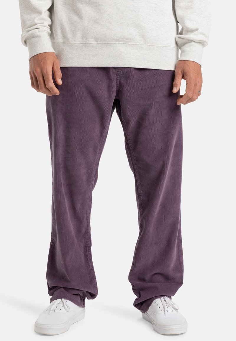 Lilla corduroy-bukser med en avslappet passform og synlig vertikal ribbing, kombinert med hvite sneakers og en lys grå hettegenser.