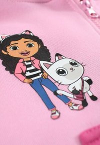 Sweatshirt rose avec une fille de dessin animé aux cheveux bouclés, portant un haut rayé et une veste rose, accompagnée d'un chat blanc avec un sac rose.