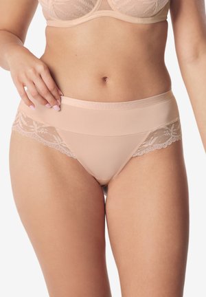 Kobieta w bieliźnie w kolorze nude, bikini z koronkową lamówką i dopasowanym biustonoszu, dłoń oparta na biodrze, widoczny tułów i górna część ud.