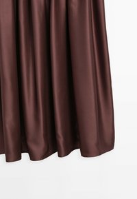 Braunes Satin-Kleid mit fließendem Design, das eine weiche Textur und einen leicht glänzenden Finish aufweist. Der Saum ist gewellt und hebt die Silhouette hervor.