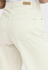 Light beige high-waisted jeans made of cotton blend fabric, featuring a branded label, two back pockets, and subtle stitching details.