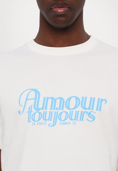 White cotton t-shirt featuring light blue graphic text reading "Amour toujours in Paris Summer 25" in a stylized font.