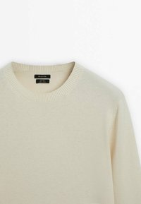 Pull col rond couleur crème avec col côtelé, en laine mérinos, présenté du haut du torse jusqu'au col sur un fond blanc.