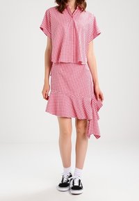 Ensemble assorti en vichy rouge et blanc avec une chemise à manches courtes et une jupe à volants. Associé à des baskets noires et des chaussettes blanches.