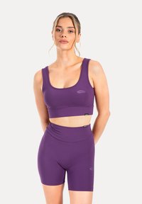 Paarse sportoutfit bestaande uit een aansluitende sportbh en high-waisted shorts, beide gemaakt van een gladde stof met minimale branding aan de voorkant.