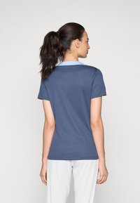 Navy blue polo shirt with a light blue collar; short sleeves and a smooth texture; fitted design, seen from the back.
