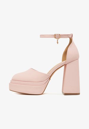 Tacones plataforma rosas con punta redondeada y tacón grueso en bloque. La correa del tobillo tiene una hebilla dorada y un detalle decorativo de cadena.