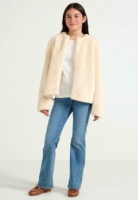 Cream-colored faux fur jacket with a relaxed fit, dropped shoulders, and no fasteners, worn over a light top and paired with blue jeans.