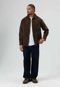 Bruine corduroy blouse met knopen, witte T-shirt eronder, gecombineerd met donkerblauwe wijde broekspijpen en bruine wandelschoenen. Eenvoudig, gestructureerd ontwerp.