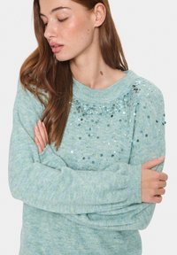 Ljusblå virkad tröja med rund halsringning och dekorationer av paljetter över den övre framsidan. Mjuk textur och avslappnad passform.