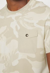 Béžové maskáčové tričko s kulatým výstřihem, krátkými rukávy a náprsní kapsou se zacvakávacím knoflíkem. Texturovaná látka.