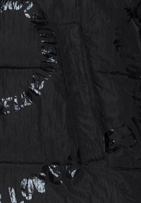 Sort puffjakke med en skinnende, struktureret overflade. Inkluderer en lynlåslomme og et trykt rundt tekstdesign i reflekterende materiale.