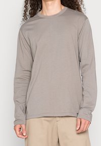 Langarmshirt in Hellgrau. Hergestellt aus weichem Stoff, zeichnet es sich durch einen klassischen Rundhalsausschnitt und minimale Nähdetails aus.
