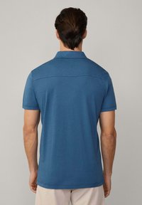 Pikétröja i blått, korta ärmar, med krage och en yoke-design på baksidan. Tillverkad av mjukt tyg med en slät textur.